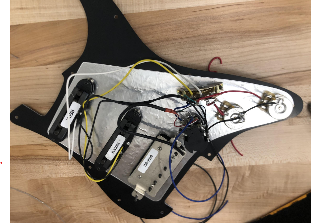 The back side of an electric guitar depicting how the electronics have been hooked up.
